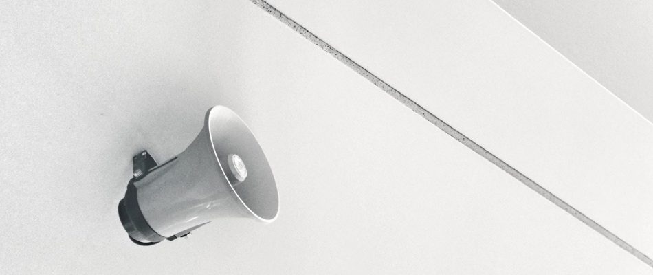 Small white speaker mounted on a white wall for business paging system.