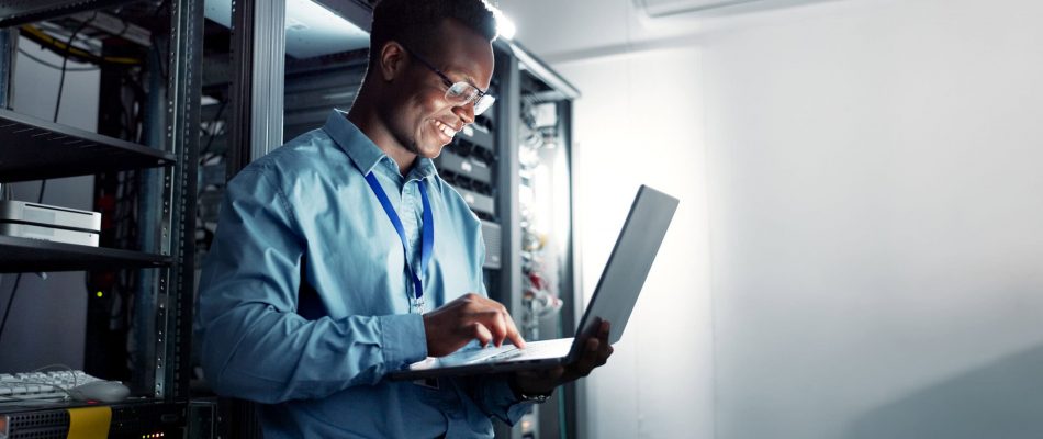 IT professional working on a laptop in a server room with data racks.