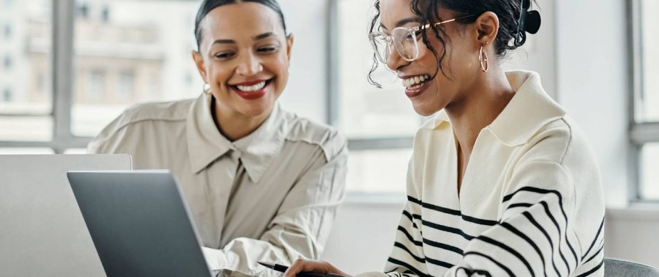 Two women collaborating on a laptop in an office setting.