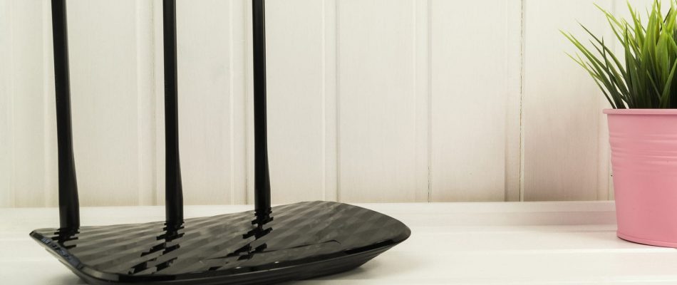 Wireless router with three antennas on a white desk in a modern office.