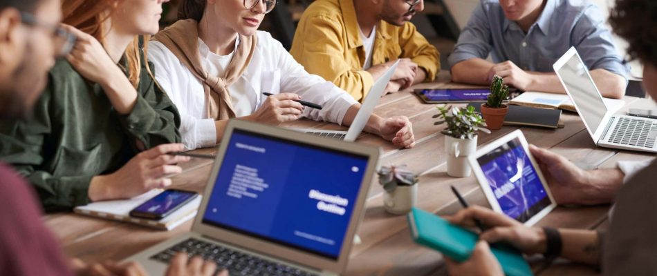 Group of diverse professionals working on laptops and tablets in a meeting room.