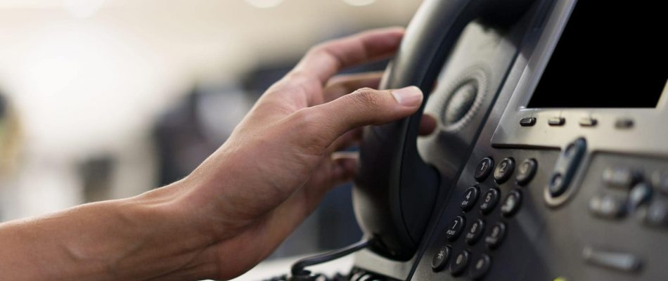 Hand dialing a business telephone with a digital display and keypad.