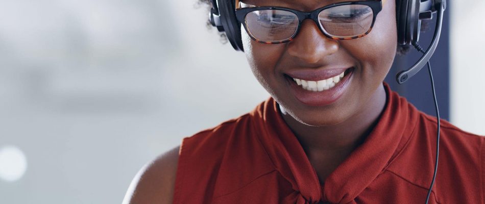 Customer support representative wearing headset and glasses smiling at computer.
